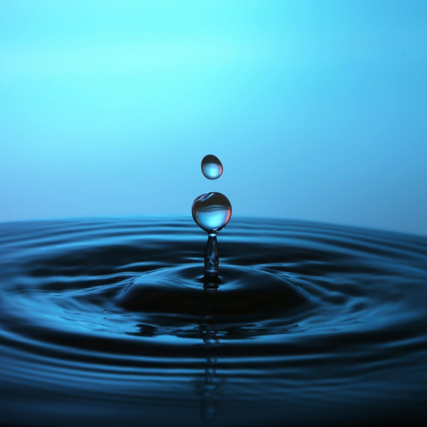 Water droplet breaking the surface and creating a splash and ripple